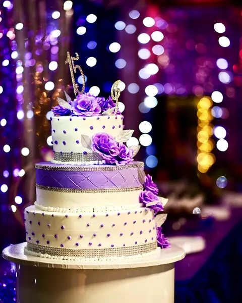 Bolo de 15 anos com flores roxas e luzes ao fundo